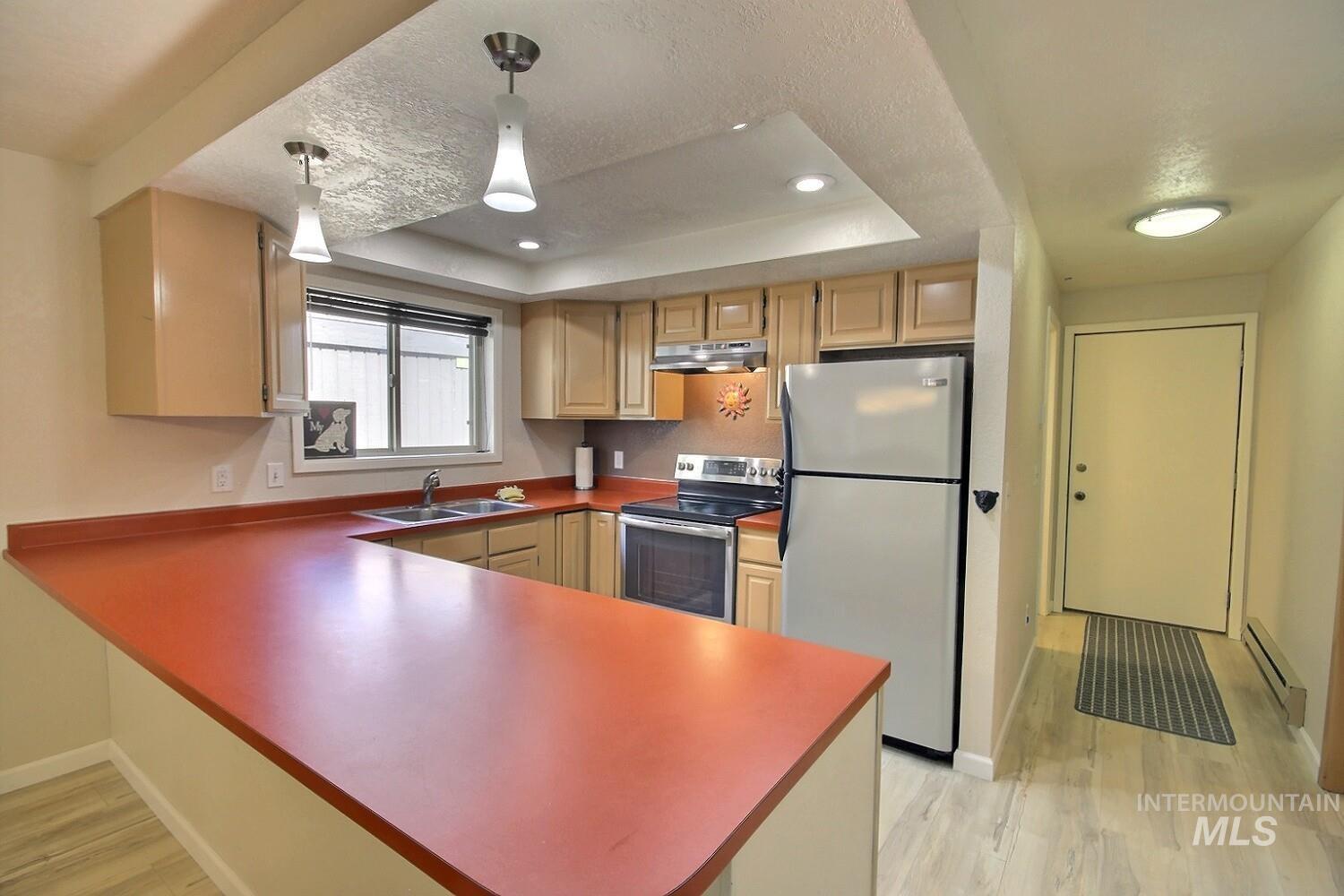 1640 Davis Avenue, Unit 7 McCall, ID 83638 - Photo 2 of 21 Kitchen featuring stainless steel appliances, a peninsula, baseboard heating, a raised ceiling, and light wood finished floors