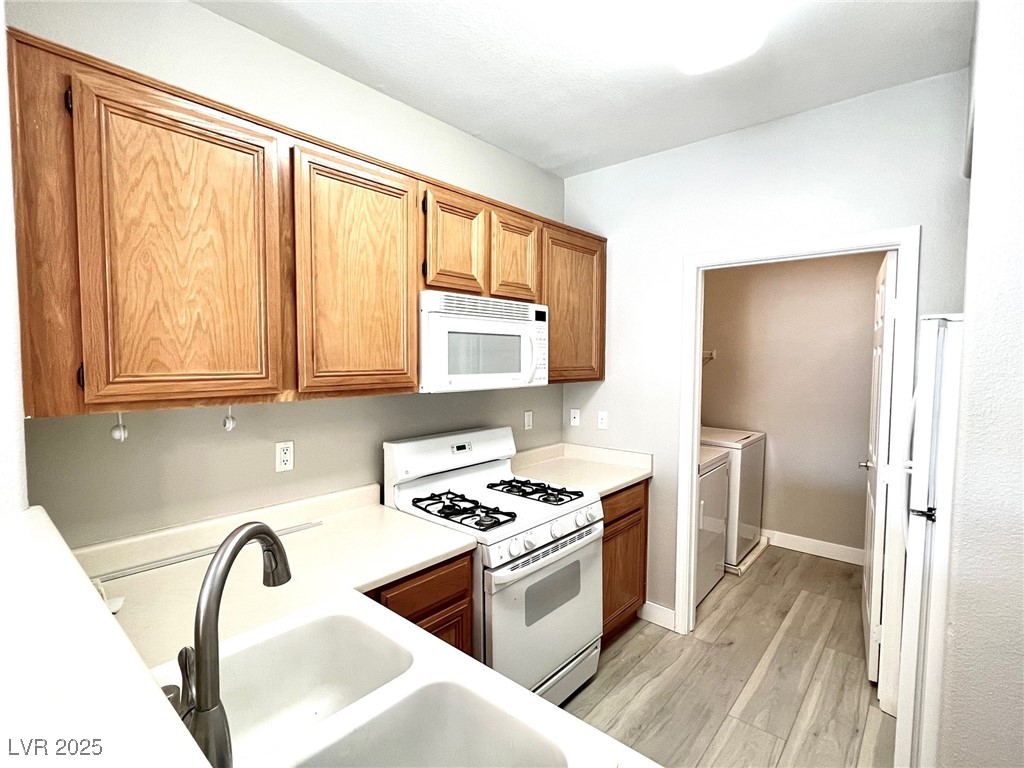7135 South Durango Drive, Unit 304 Las Vegas, NV 89113 - Photo 6 of 11 Kitchen featuring white appliances, washer and clothes dryer, light wood-type flooring, light countertops, and brown cabinetry