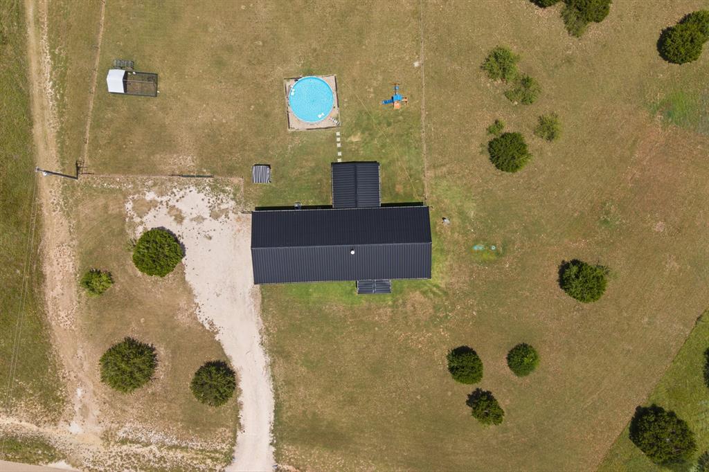 1031 Augustus Court Rio Vista, TX 76093 - Photo 25 of 30 Expansive property featuring a dark-roofed structure, large grassy areas, an above-ground pool, a gravel driveway, and scattered mature trees