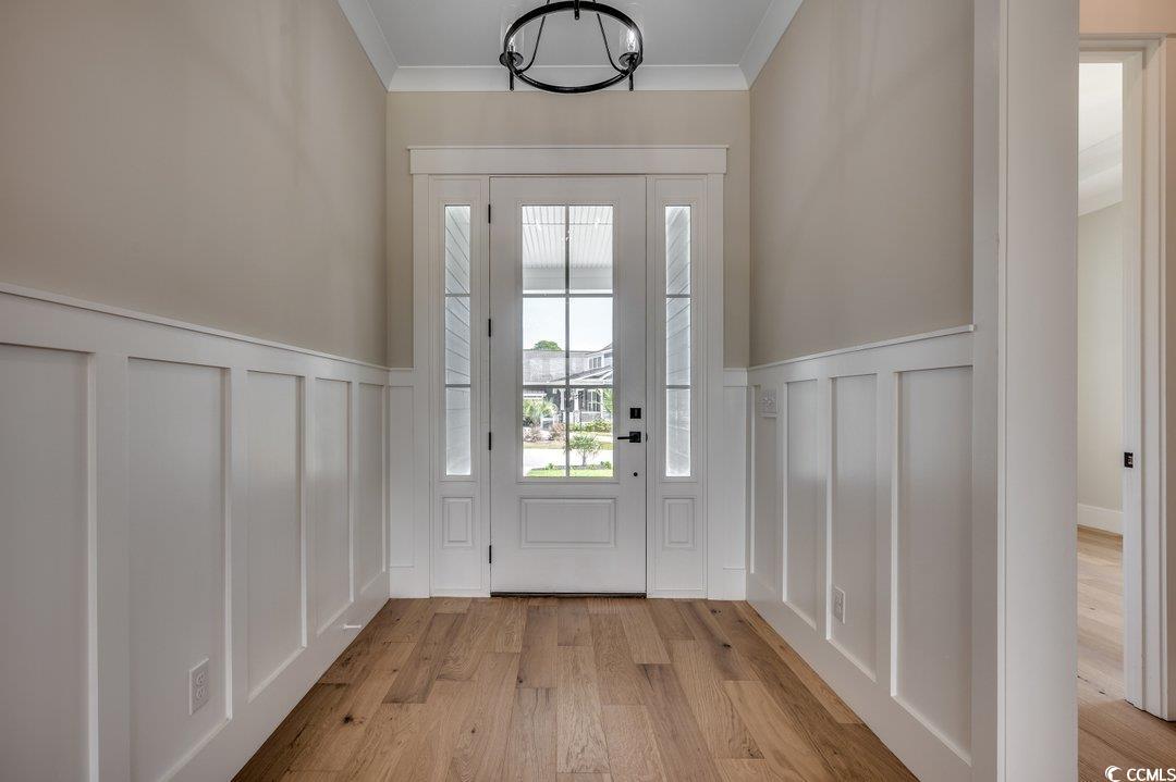 404 Plantation Oaks Drive Myrtle Beach, SC 29579 - Photo 14 of 29 Doorway to outside featuring a decorative wall, light wood-style floors, a wainscoted wall, ornamental molding, and a chandelier
