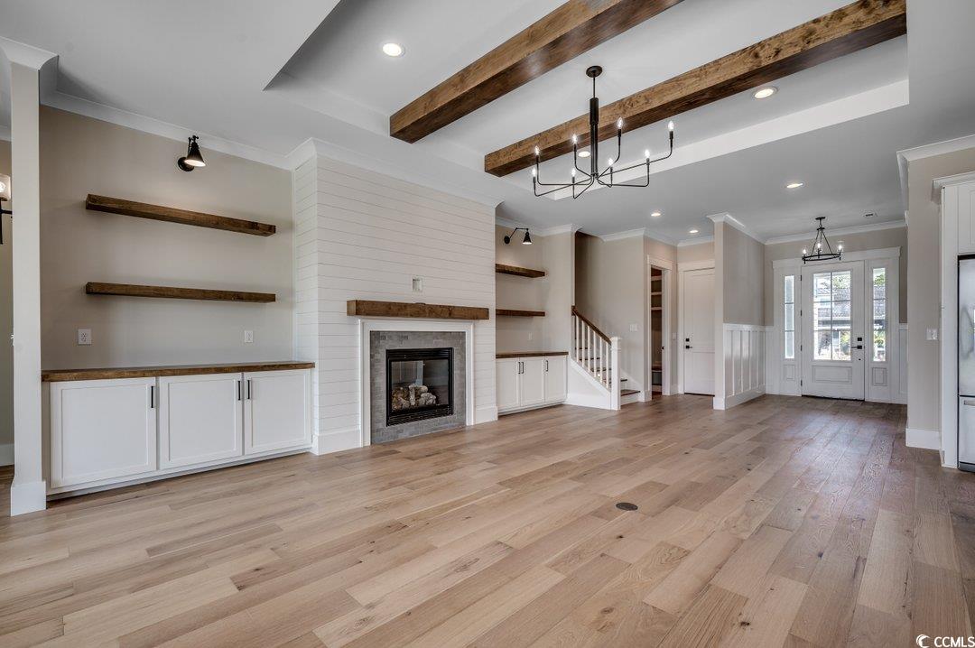 404 Plantation Oaks Drive Myrtle Beach, SC 29579 - Photo 4 of 29 Unfurnished living room featuring a chandelier, light wood-style floors, beam ceiling, crown molding, and a glass covered fireplace