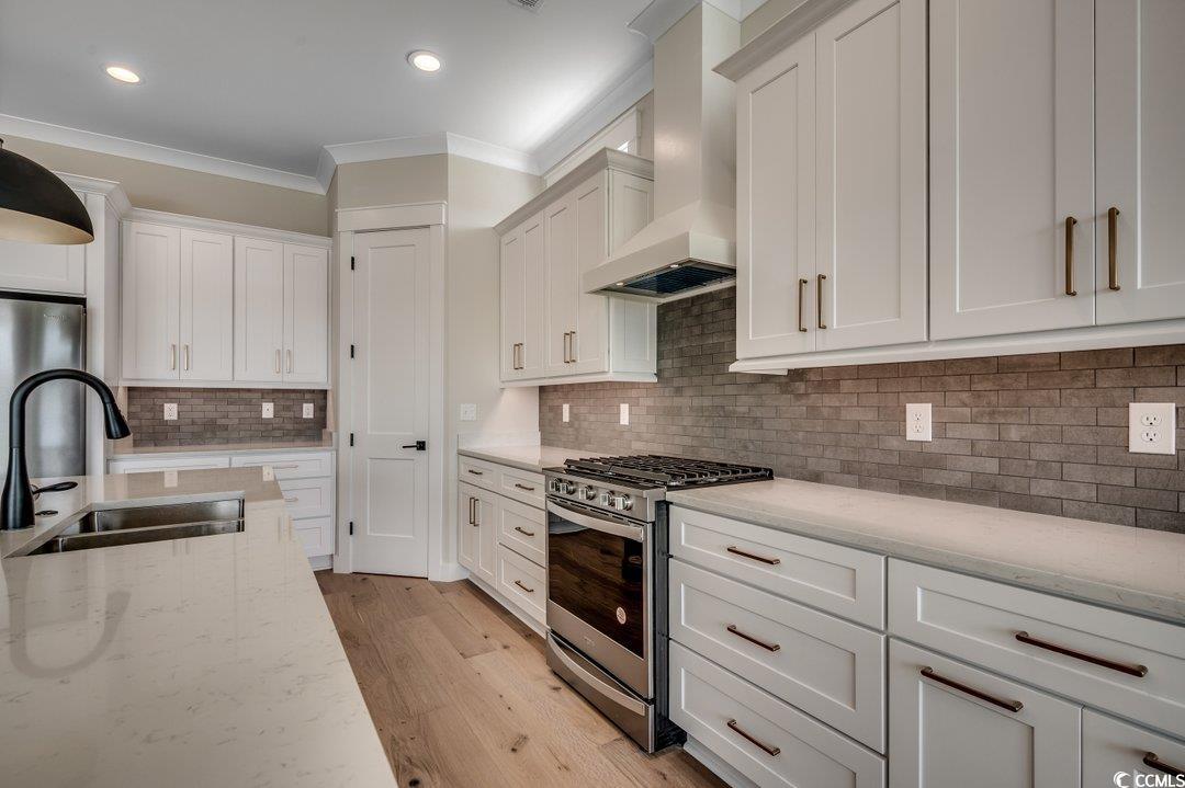 404 Plantation Oaks Drive Myrtle Beach, SC 29579 - Photo 7 of 29 Kitchen with stainless steel appliances, a sink, ornamental molding, wall chimney range hood, and decorative backsplash