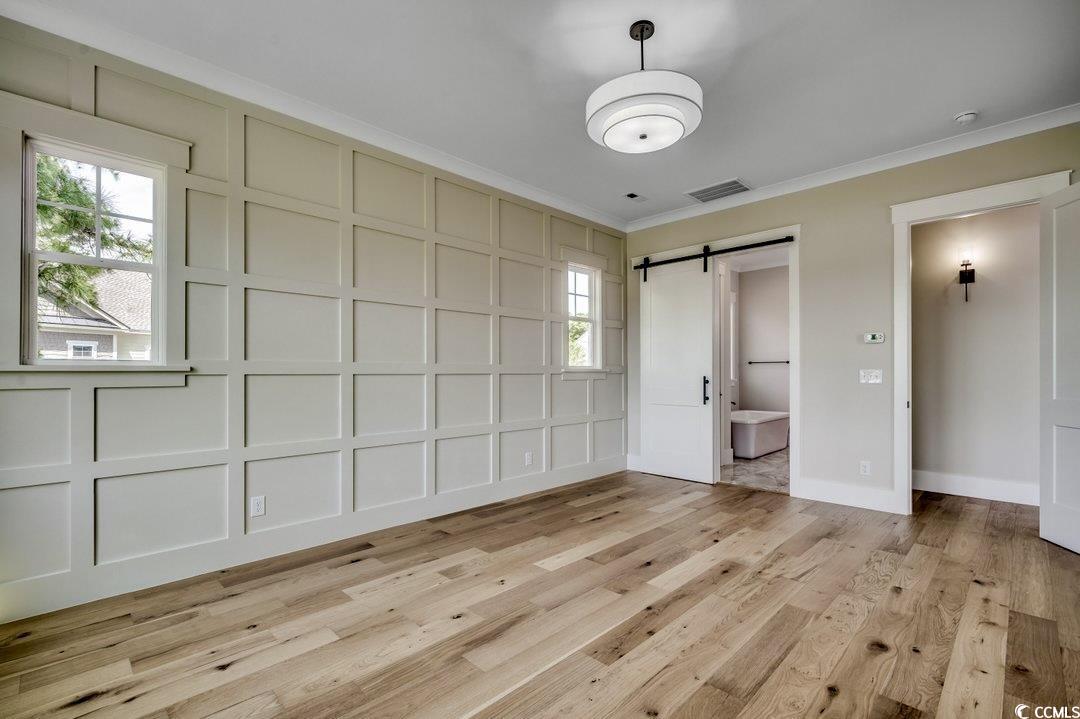 404 Plantation Oaks Drive Myrtle Beach, SC 29579 - Photo 8 of 29 Unfurnished bedroom featuring crown molding, a barn door, a decorative wall, multiple windows, and light wood finished floors