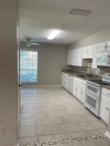 a large kitchen with granite countertop a stove a sink a window and white cabinets
