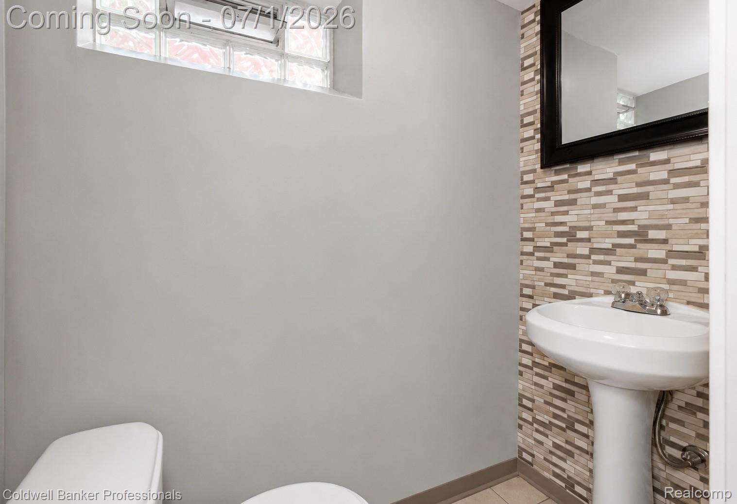 1168 Vernier Road Grosse Pointe, MI 48236 - Photo 24 of 32 Pedestal sink with chrome faucet, complemented by a multi-tone tile accent wall and a rectangular mirror with a black frame