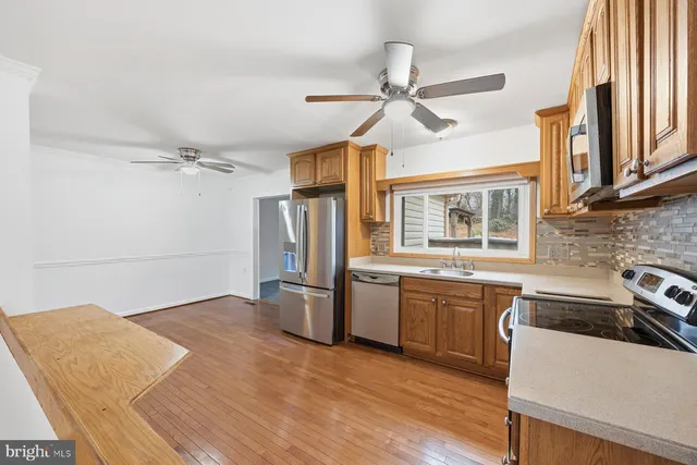 a kitchen with stainless steel appliances granite countertop a refrigerator a sink dishwasher a stove and white countertops with wooden floor