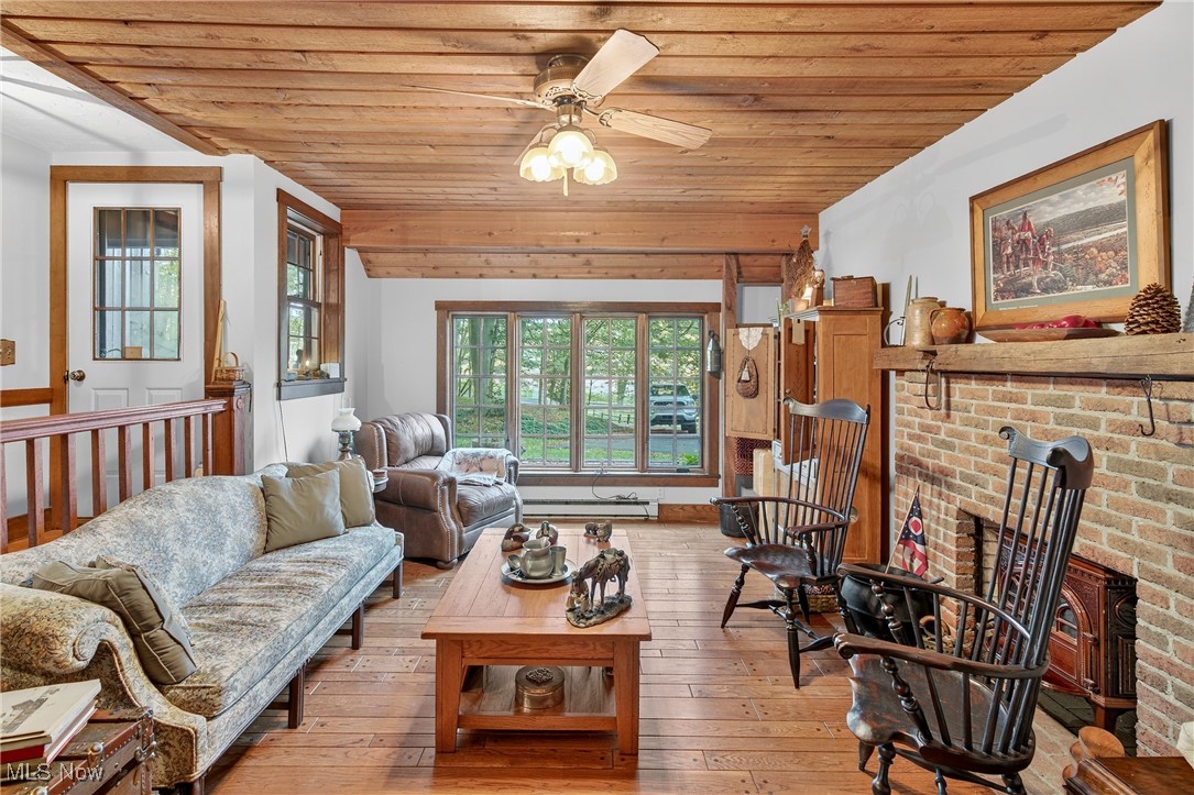 25700 Winona Road Homeworth, OH 44634 - Photo 5 of 49 Den area with wood ceiling, light wood-style floors, a ceiling fan, a brick fireplace, and a baseboard radiator