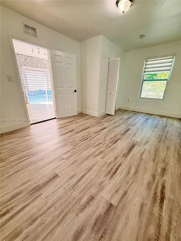 a view of an empty room with wooden floor and a window