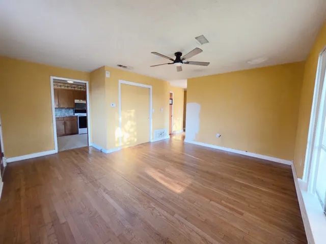 a view of an empty room with wooden floor and a ceiling fan