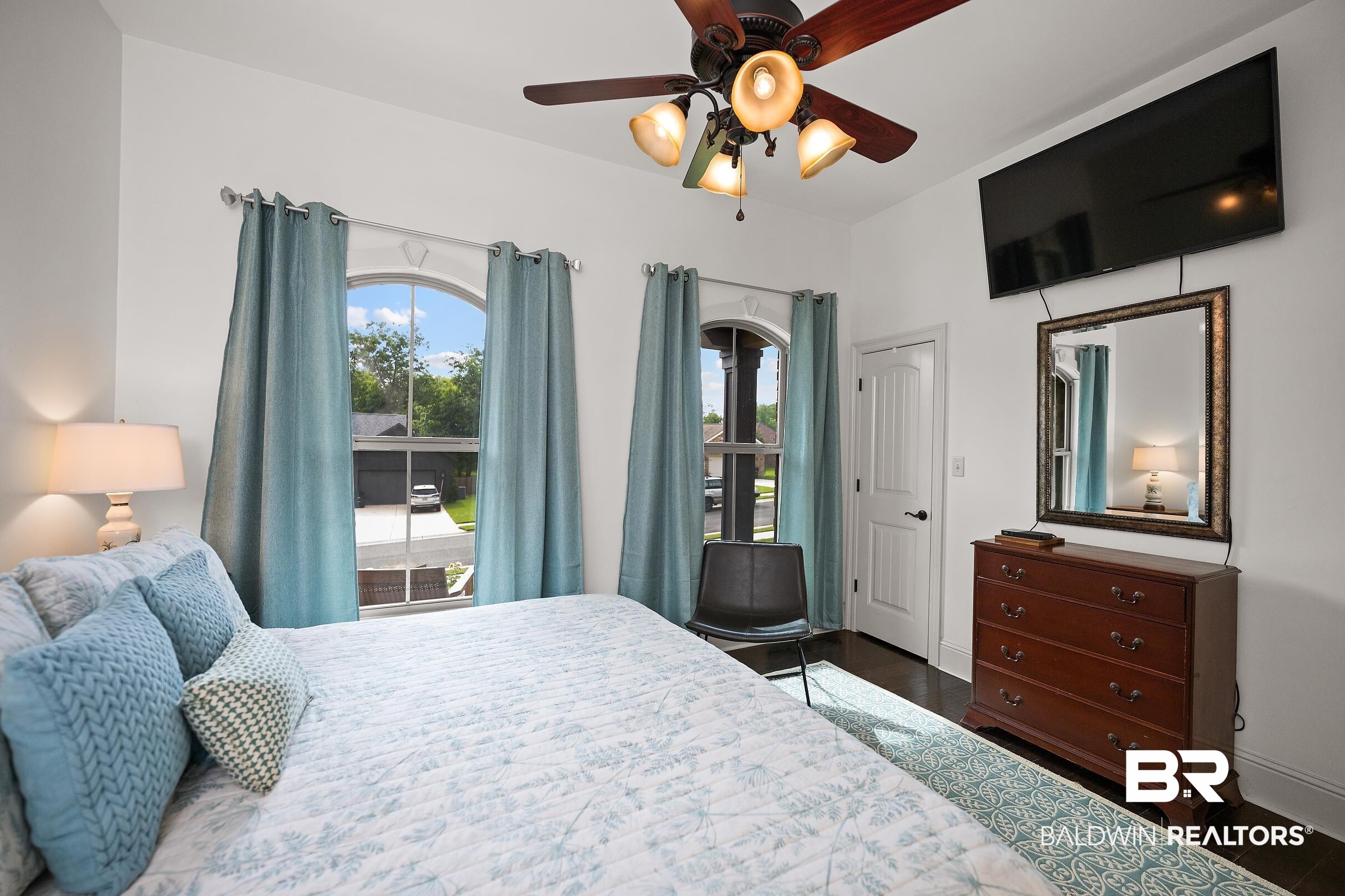313 Pecan Ridge Boulevard Fairhope, AL 36532 - Photo 18 of 51 Bedroom featuring a ceiling fan with integrated lighting, two arched windows, dark wood-finish flooring, and white painted trim