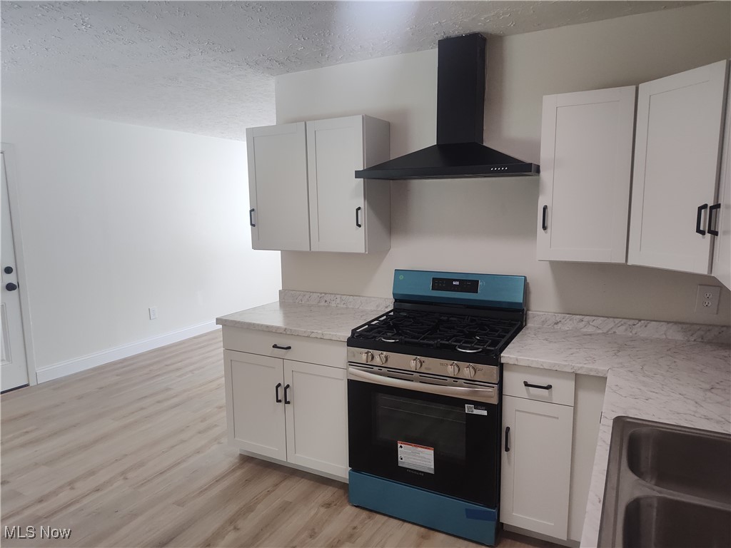 8016 Ninevah Road Geneva, OH 44041 - Photo 26 of 45 Kitchen featuring stainless steel gas stove, a textured ceiling, wall chimney range hood, white cabinetry, and light wood finished floors