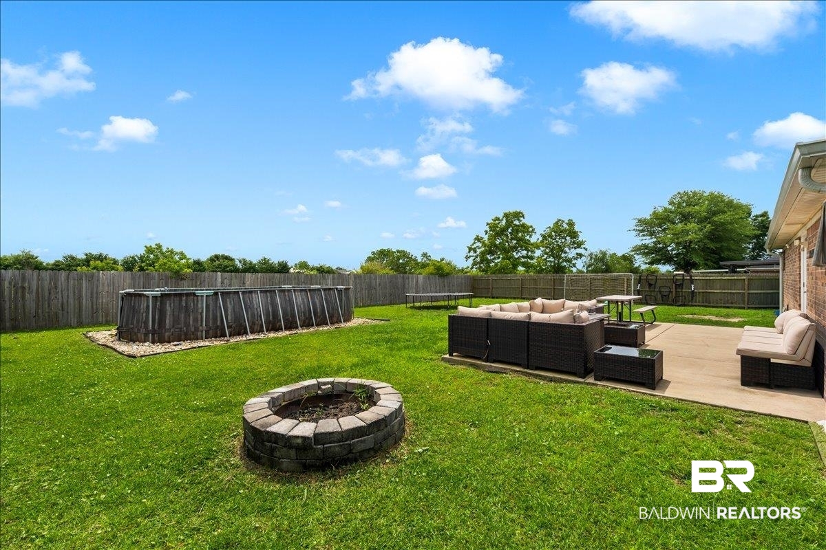 8952 Sherman Road Foley, AL 36535 - Photo 35 of 41 Expansive backyard featuring a rectangular above-ground pool, a stone-block fire pit, a concrete patio, and a privacy fence