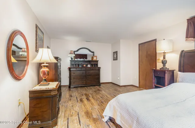 a bedroom with a bed a dresser and potted plants with wooden floor