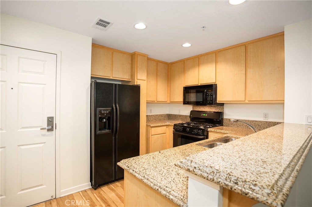 160 South Hudson Avenue, Unit 303 Pasadena, CA 91101 - Photo 4 of 14 a kitchen with granite countertop wooden cabinets a refrigerator and a sink