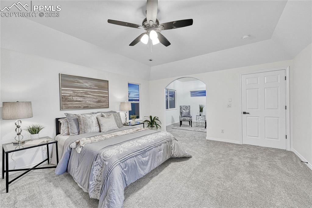 1185 Bowstring Road Monument, CO 80132 - Photo 22 of 46 a spacious bedroom with a bed a chandelier and a window