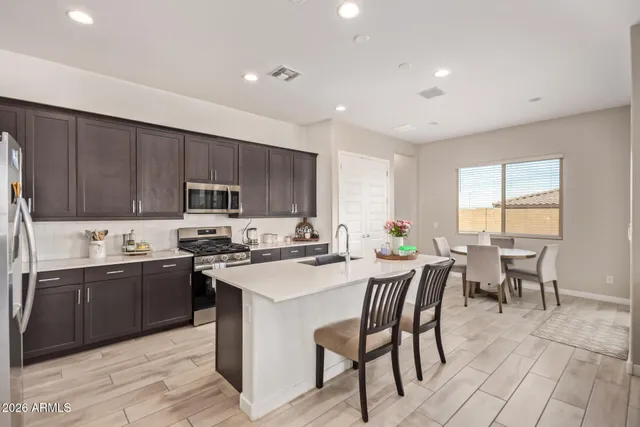 a kitchen with stainless steel appliances granite countertop a stove a sink a refrigerator a dining table and chairs