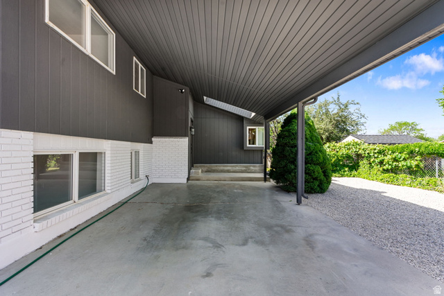 432 Calnette Drive Sandy, UT 84070 - Photo 46 of 48 Carport entrance featuring a concrete drive, white brick foundation, dark vertical siding, and a gravel pathway
