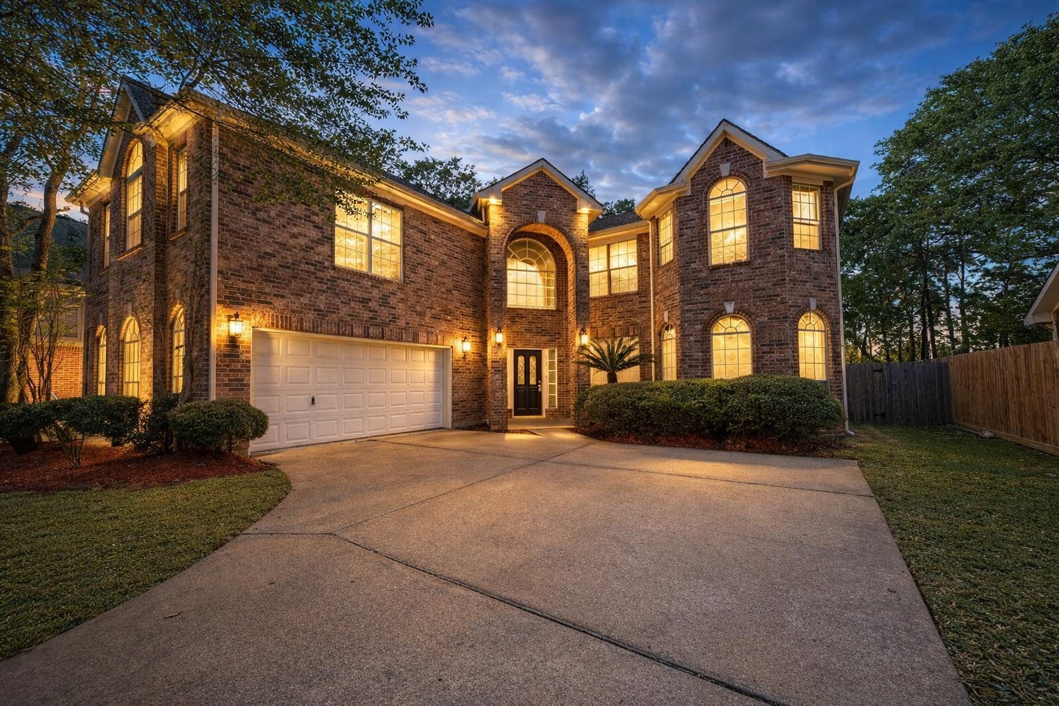 This stunning brick facade home boasts charming arched windows, lush greenery, and a welcoming driveway, offering a perfect blend of elegance and comfort.