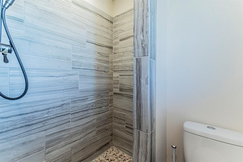 708 North Stewart Street Azle, TX 76020 - Photo 15 of 25 Walk-in shower with updated tile surround and pebble-style flooring.