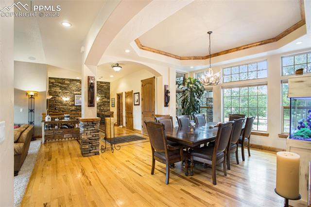 11628 Shaugnessy Road Colorado Springs, CO 80908 - Photo 9 of 50 Dining area with light hardwood / wood-style floors, a tray ceiling, and a notable chandelier