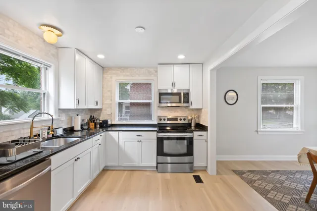 a kitchen with stainless steel appliances granite countertop a stove a sink dishwasher a refrigerator and white cabinets with wooden floor