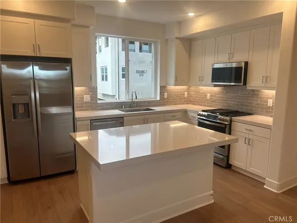 a kitchen with stainless steel appliances granite countertop a refrigerator a stove and a sink with wooden floor