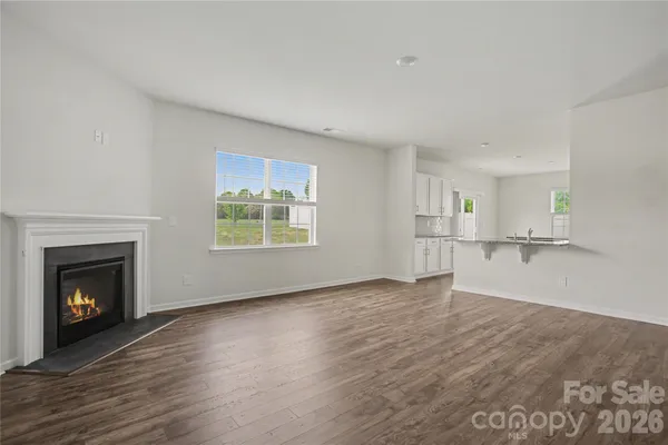 a view of an empty room with wooden floor fireplace and a window