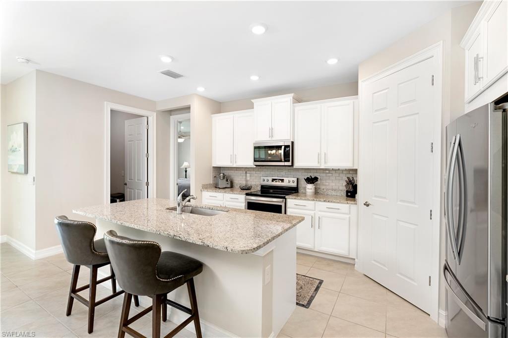 14488 Stillwater Way Naples, FL 34114 - Photo 6 of 36 Kitchen featuring stainless steel appliances, light tile patterned floors, an island with sink, white cabinets, and recessed lighting