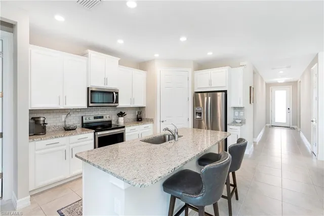 a kitchen with stainless steel appliances granite countertop a sink a stove a refrigerator cabinets and a dining table with wooden floor