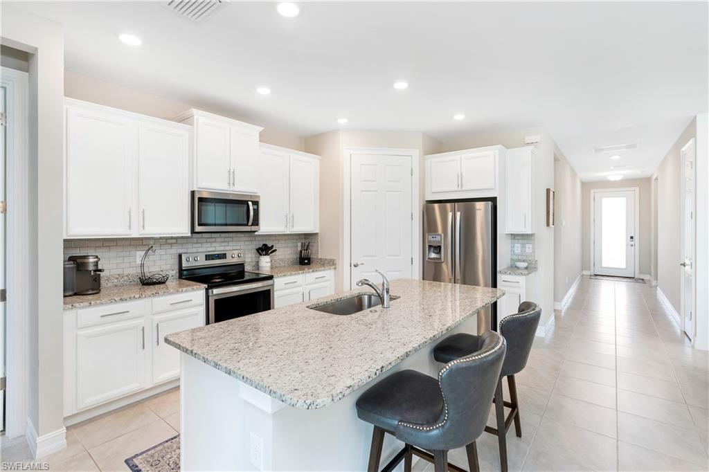 14488 Stillwater Way Naples, FL 34114 - Photo 7 of 36 Kitchen with stainless steel appliances, white cabinetry, tasteful backsplash, light stone counters, and light tile patterned floors