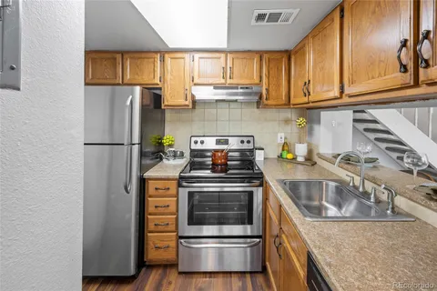 a kitchen with stainless steel appliances granite countertop a stove a refrigerator and a sink with wooden cabinets