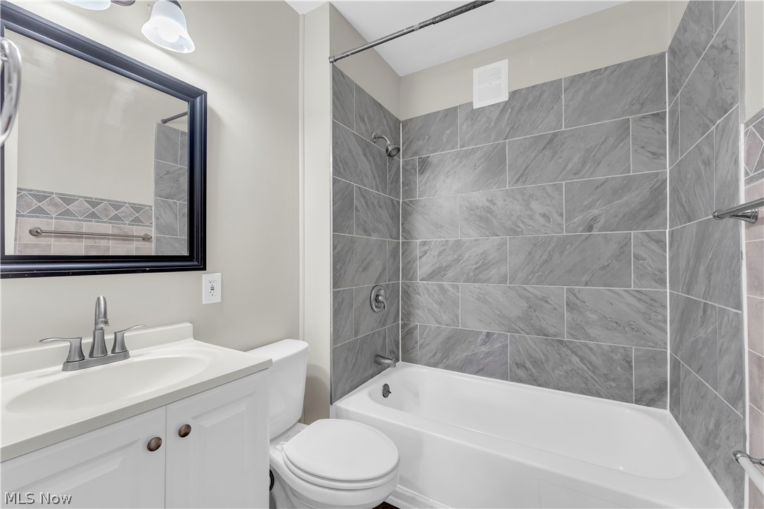 18123 McCracken Road Maple Heights, OH 44137 - Photo 22 of 27 Bathroom featuring a white vanity with silver hardware, a rectangular mirror with a black frame, a toilet, a bathtub with a shower, and gray subway-style tile in the shower surround