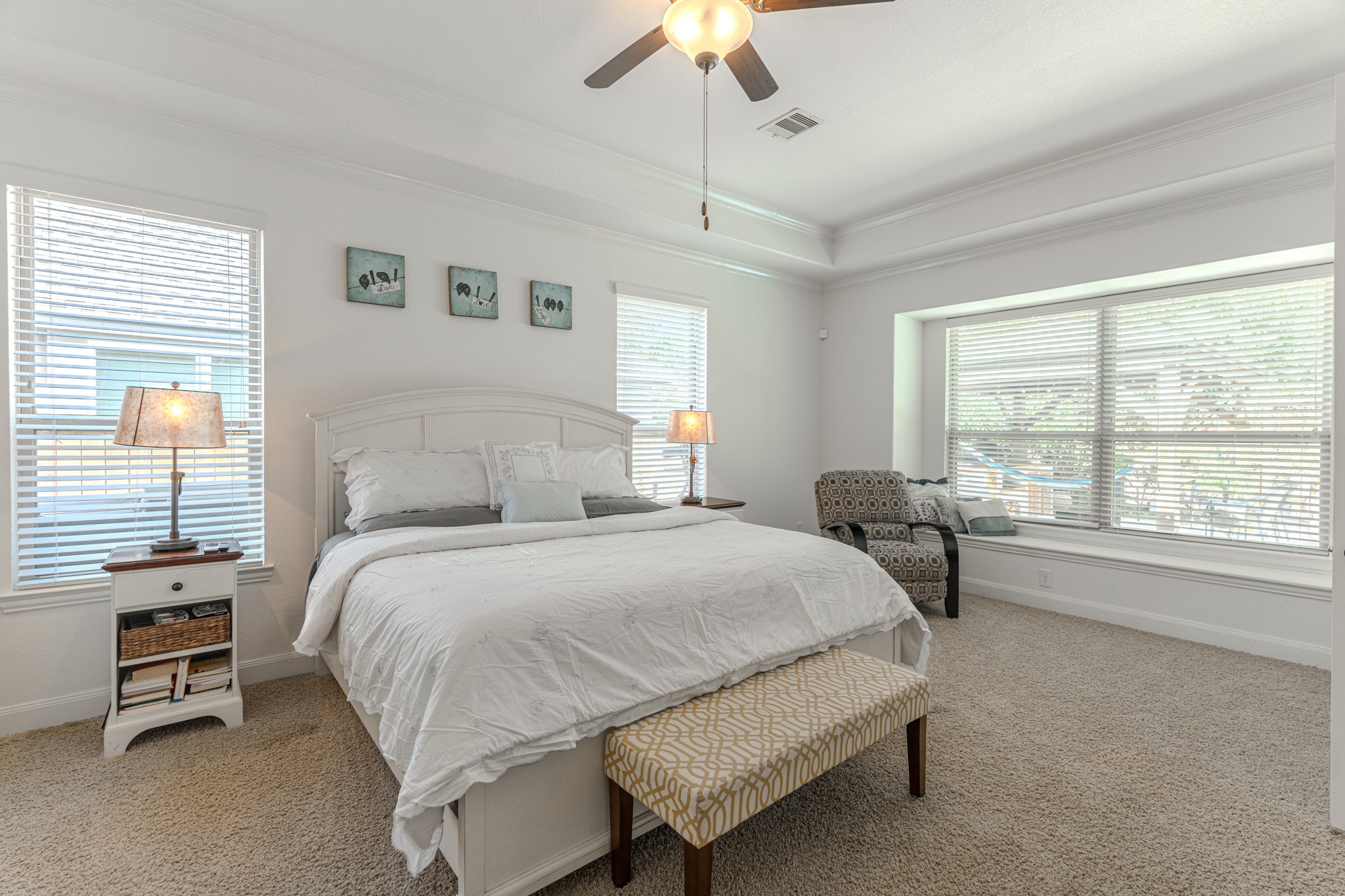 30 Fury Ranch Place The Woodlands, TX 77375 - Photo 26 of 47 Bright and inviting bedroom featuring a comfortable bed, ceiling fan, and soft carpeting. The room is well-lit with natural light from two windows and includes tasteful decor. There's a private en-suite bathroom visible through an open door, adding convenience and luxury.