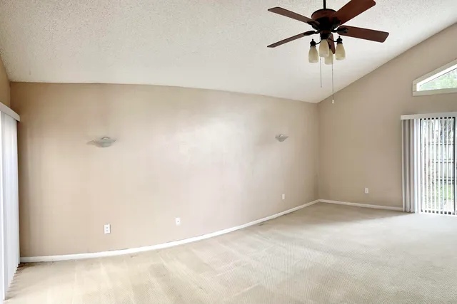 an empty room with chandelier fan and windows