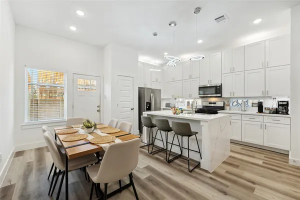 a kitchen with kitchen island granite countertop a dining table chairs refrigerator and cabinets