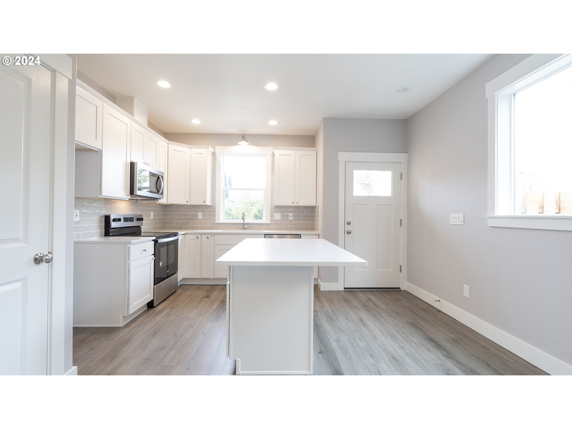 6921 Southeast Pardee Street, Unit A Portland, OR 97206 - Photo 5 of 16 a open kitchen with white cabinets a sink dishwasher and a stove with wooden floor