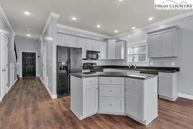 a kitchen with stainless steel appliances granite countertop a refrigerator a sink dishwasher a stove and white cabinets with wooden floor