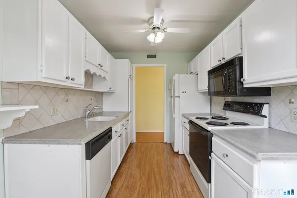 a kitchen with stainless steel appliances granite countertop a sink a stove top oven a refrigerator with white cabinets and couches
