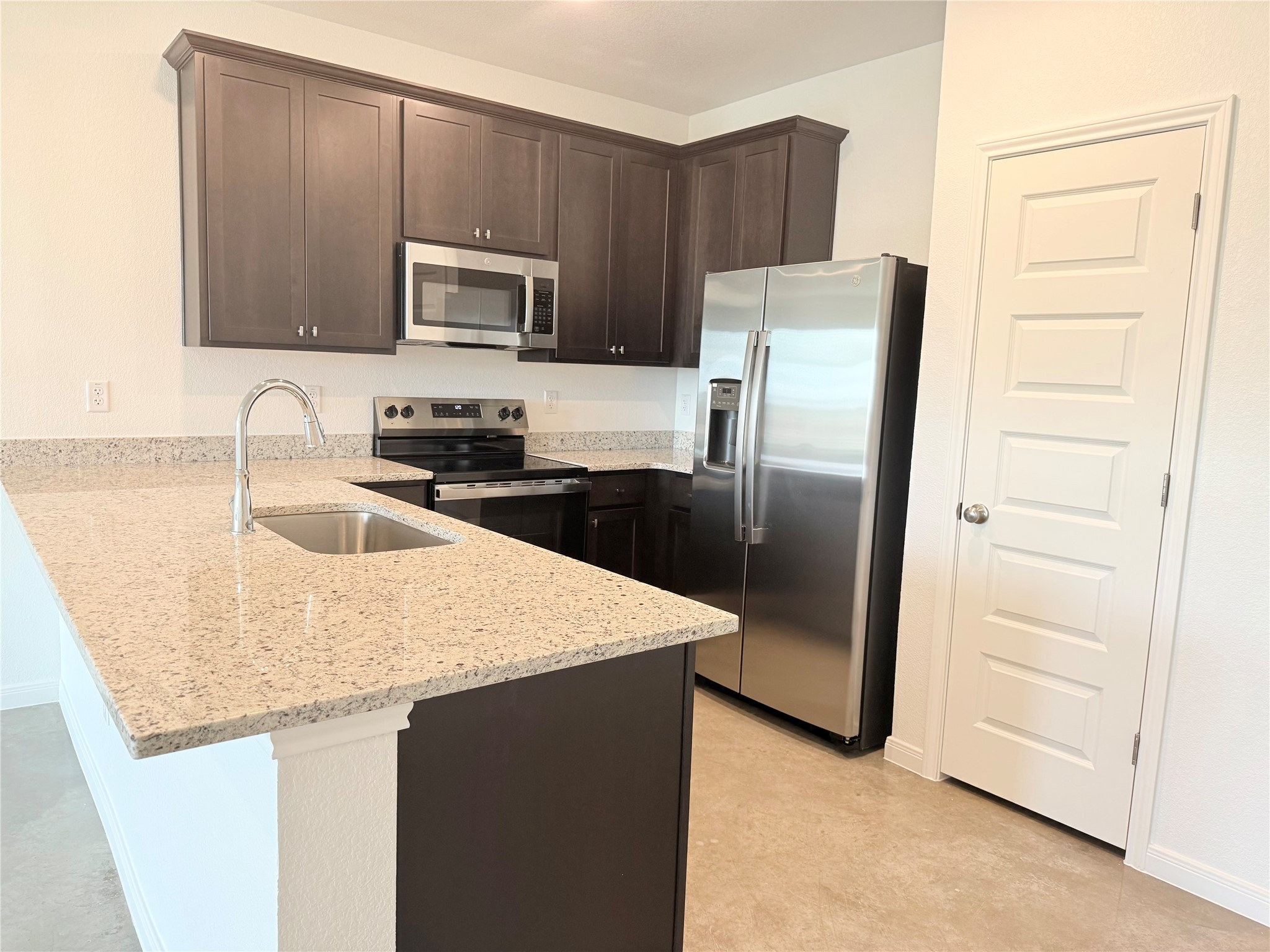 2909 Quail Rdg Lane, Unit A Temple, TX 76501 - Photo 5 of 19 Kitchen with dark wood finish cabinetry, stainless steel appliances, a peninsula, light stone counters, and a kitchen bar