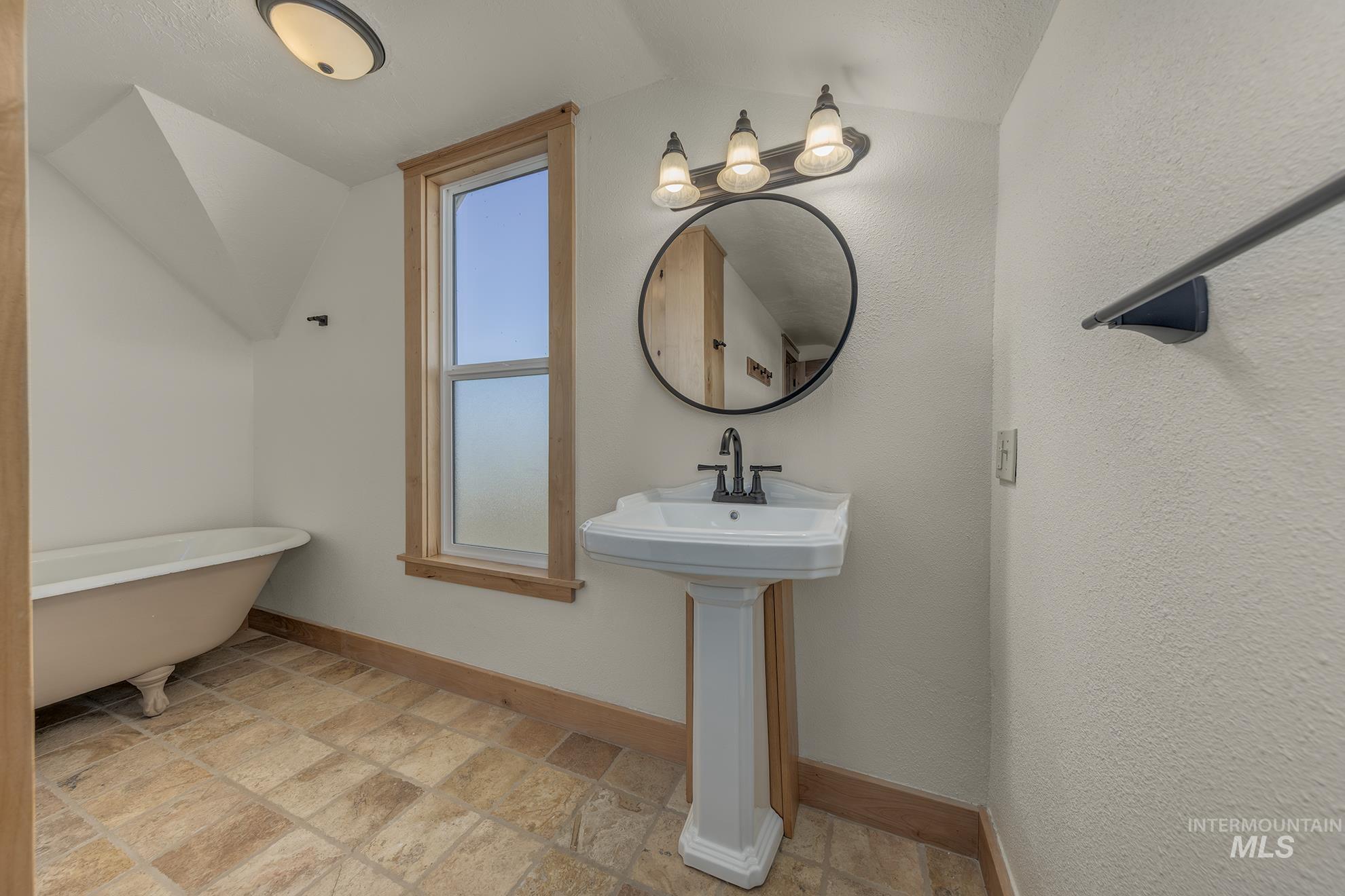 327 Macomb Road Weiser, ID 83672 - Photo 28 of 49 Bathroom featuring stone tile floors, a freestanding tub, vaulted ceiling, and a textured wall