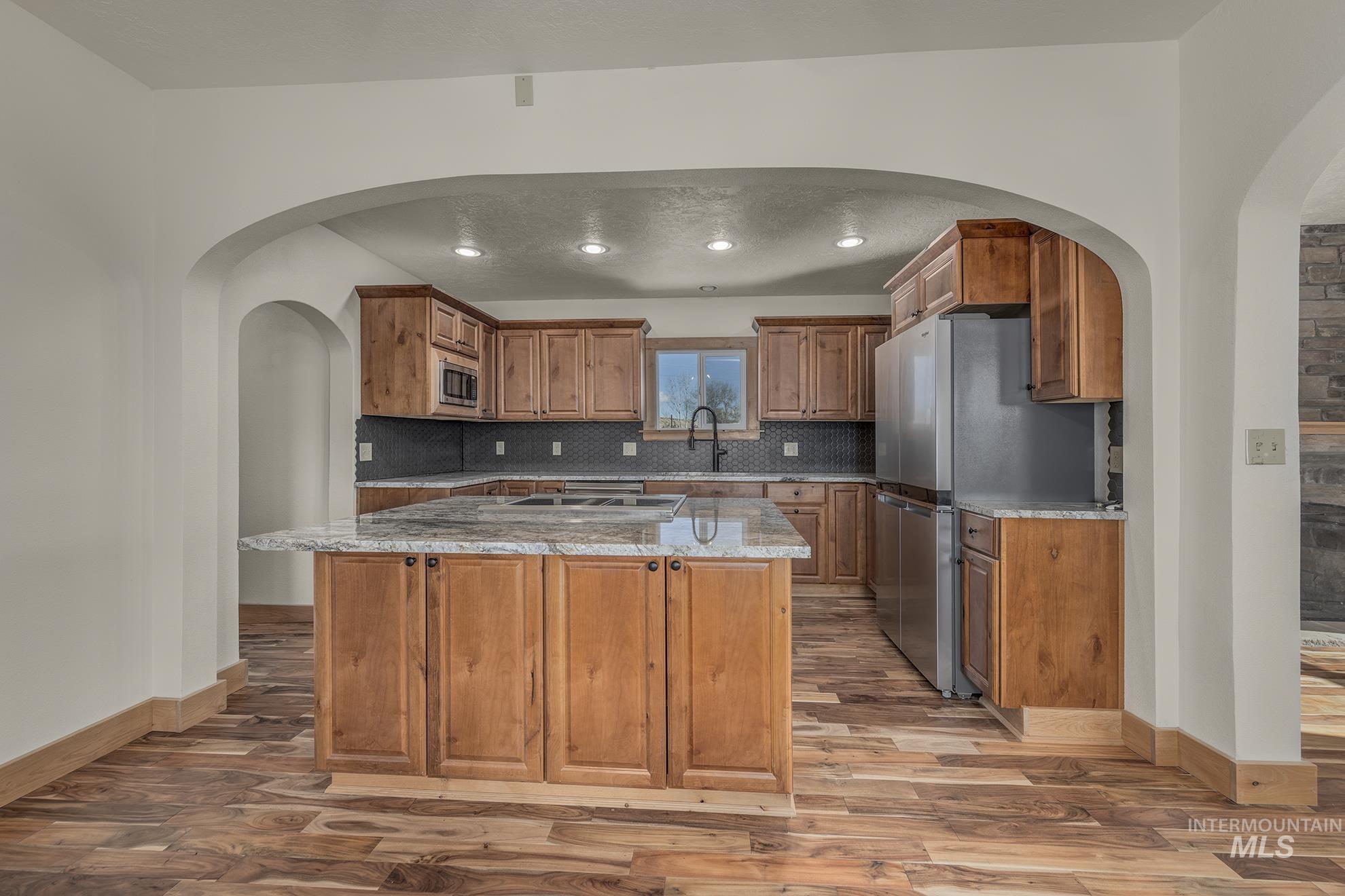327 Macomb Road Weiser, ID 83672 - Photo 10 of 49 Kitchen with arched walkways, brown cabinetry, light stone countertops, stainless steel appliances, and a center island