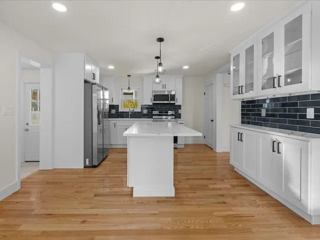 a large kitchen with stainless steel appliances kitchen island a stove a refrigerator a sink dishwasher and white cabinets with wooden floor