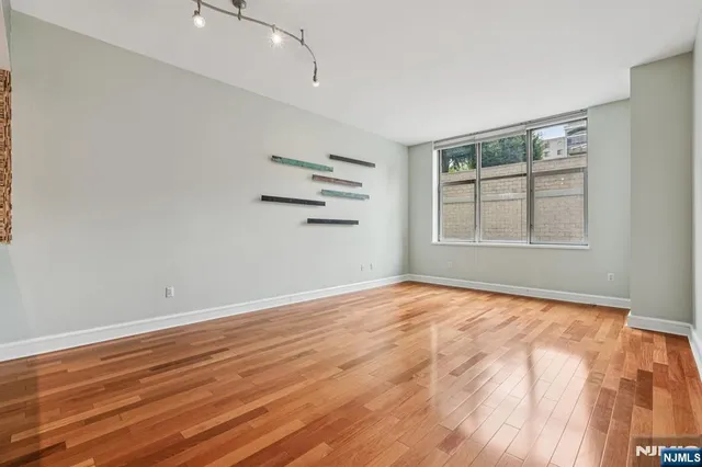 a view of an empty room with wooden floor and a kitchen