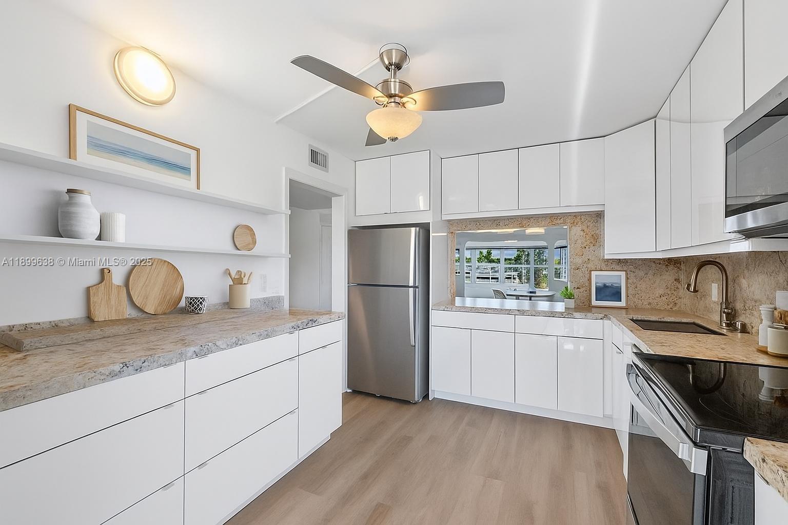 a kitchen with stainless steel appliances granite countertop a sink stove a refrigerator and white cabinets with wooden floor