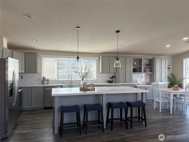 a kitchen with stainless steel appliances granite countertop a dining table chairs and wooden floor