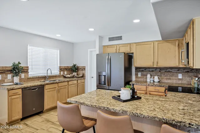 a kitchen with stainless steel appliances kitchen island granite countertop a refrigerator a stove top oven a sink dishwasher and wooden cabinets with wooden floor