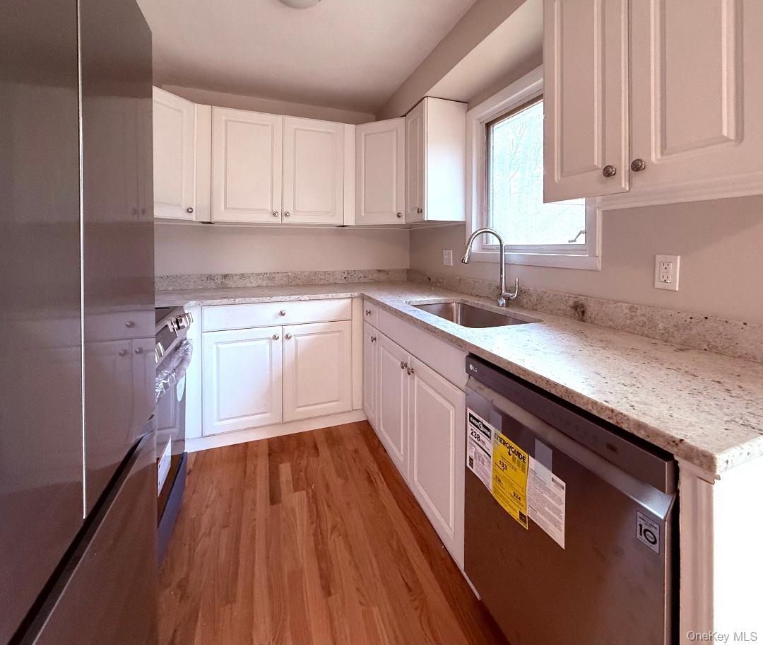 Kitchen featuring sink, white cabinetry, light stone countertops, light hardwood / wood-style floors, and stainless steel appliances