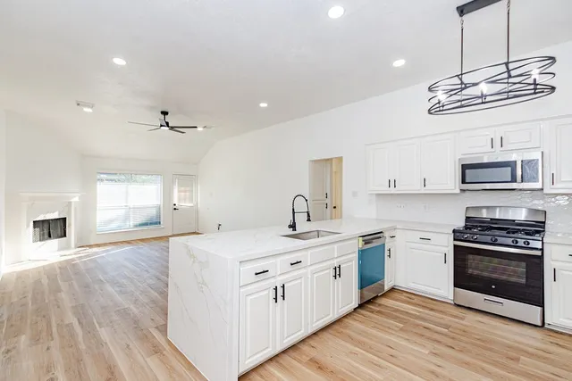 a kitchen with a sink stainless steel appliances a stove cabinets and wooden floor
