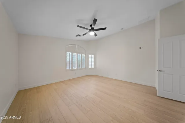 an empty room with wooden floor ceiling fan and windows