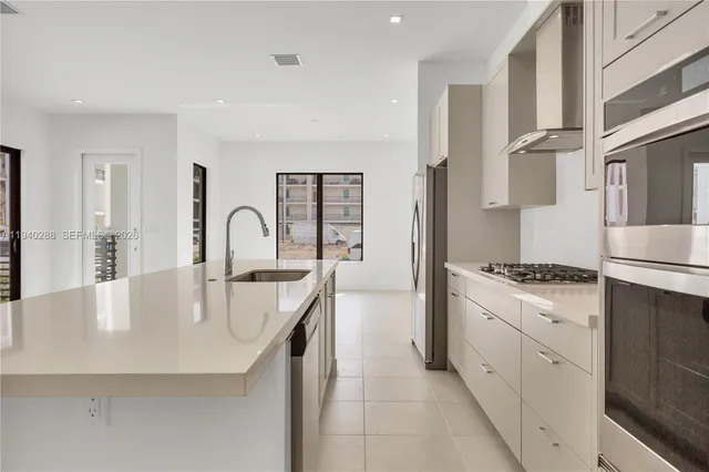 a large white kitchen with stainless steel appliances granite countertop a stove a sink a refrigerator and white cabinets next to a window